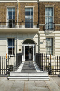 EIFA Front view of a traditional London townhouse with a symmetrical facade, brick upper walls, and a white lower section. It features large windows, a black iron fence, and stairs leading to a glossy black door with side windows, embodying the citys bilingual charm.