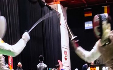 EIFA Two fencers in protective gear and masks compete on a platform, surrounded by flags from various countries. The indoor scene, akin to an intense treasure hunt at the National Gallery, unfolds against a dark curtain, emphasizing the duel between the athletes.