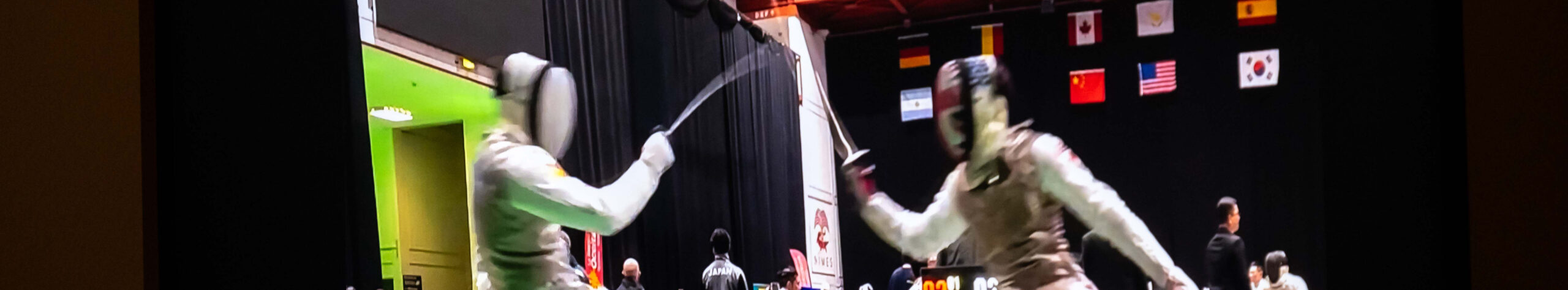 EIFA Two fencers in protective gear and masks compete on a platform, surrounded by flags from various countries. The indoor scene, akin to an intense treasure hunt at the National Gallery, unfolds against a dark curtain, emphasizing the duel between the athletes.